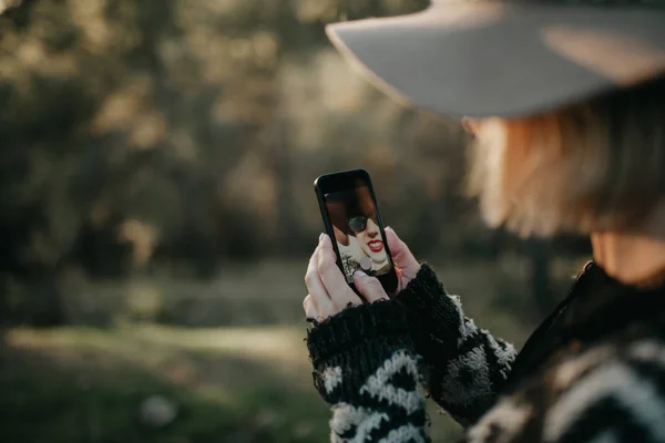 Kvinna tar ett foto med en mobiltelefon i naturen. Hon syns i skärmen genom enhetens främre kamera. — Stockfoto