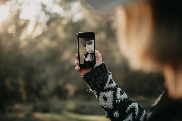 Woman taking a photo with a mobile phone in nature. She appears in the screen through the device frontal camera.