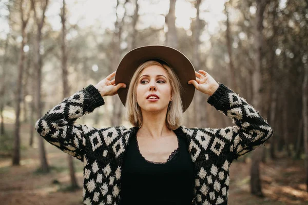 Portrait of blonde white woman putting on a hat in the forest. — Stock Photo, Image