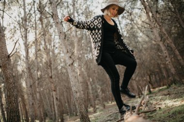 Düşmüş ağaç gövdesi ormanda yürürken rahat kıyafetler içinde gülümseyen kadın