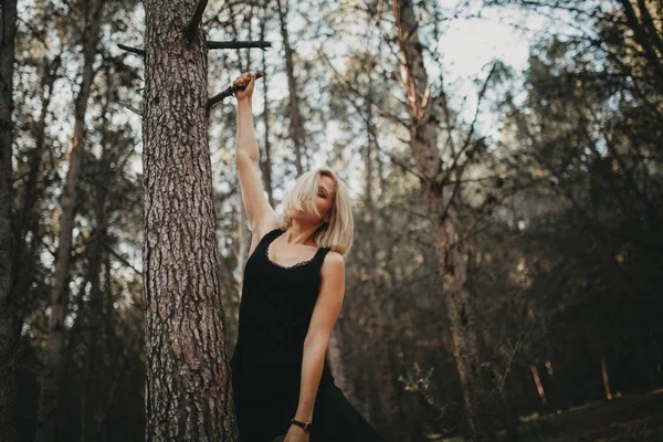 Blonde vrouw opknoping van een vertakking van de beslissingsstructuur van het pine in het bos. — Stockfoto