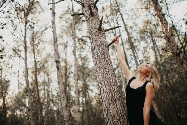 Blonde vrouw opknoping van een vertakking van de beslissingsstructuur van het pine in het bos. — Stockfoto