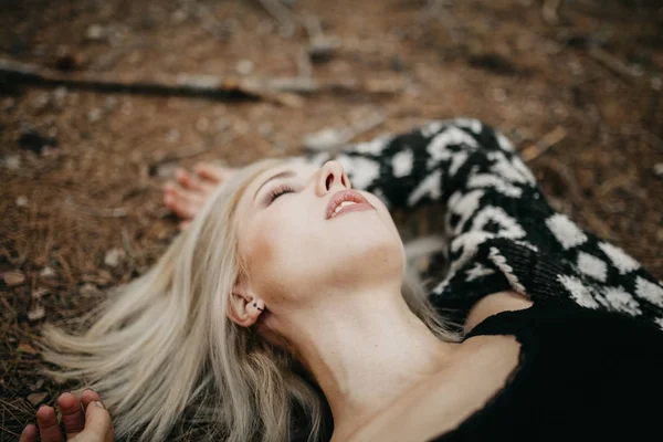 Cute blonde woman lying down on the forest ground.