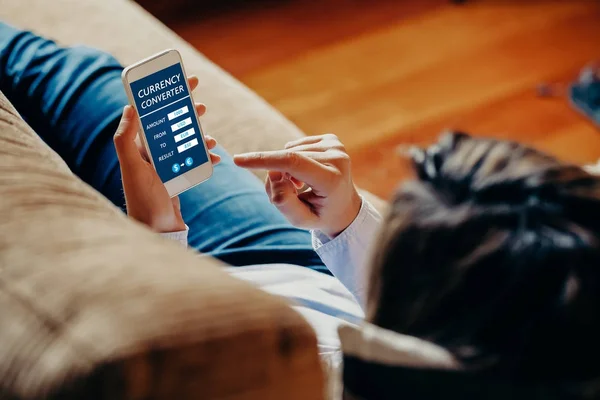 Mujer usando un convertidor de moneda de teléfono móvil mientras está sentado en casa . — Foto de Stock