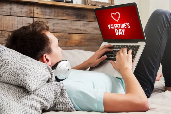 Evde yatakta dinlenme sırasında hediyeler için adam bir Sevgililer günü alışveriş Web sitesi ziyaret — Stok fotoğraf