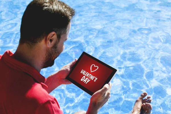 Hombre de compras regalos de San Valentín con una tableta digital mientras está sentado en la piscina al aire libre . — Foto de Stock
