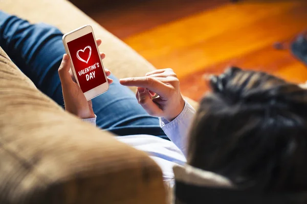 Mujer sosteniendo un teléfono móvil con la aplicación de compras del día de San Valentín en la pantalla en casa . — Foto de Stock