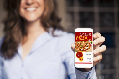 Pizza alışveriş uygulaması ile hareket eden telefon içinde belgili tanımlık perde tutan gülümseyen kadın.