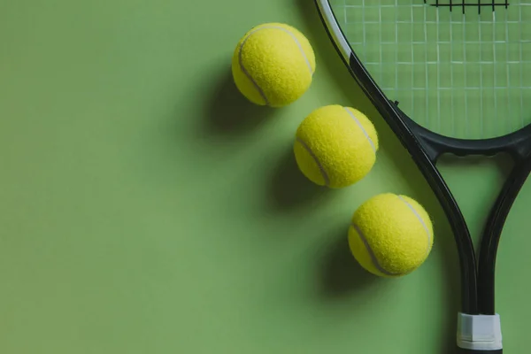 Drei Tennisbälle und ein Tennisschläger auf grünem Hintergrund, mit Kopierraum. — Stockfoto