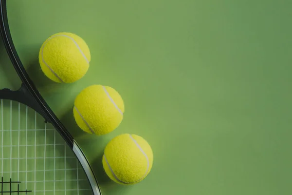 Три теннисных мяча и теннисная ракетка на зеленом фоне с копировальным пространством справа . — стоковое фото