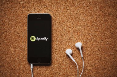 Malaga, İspanya - 5 Mart 2018: cep telefonu Spotify logolu bir mantar panelde yerleştirilmiş ekran ve beyaz kulaklık.