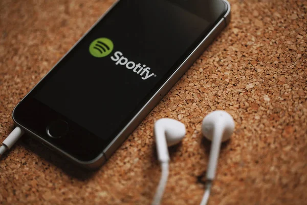 MALAGA, ESPAÑA - 5 DE MARZO DE 2018: Teléfono móvil con logotipo de Spotify en la pantalla y auriculares blancos, colocado en un panel de corcho . —  Fotos de Stock