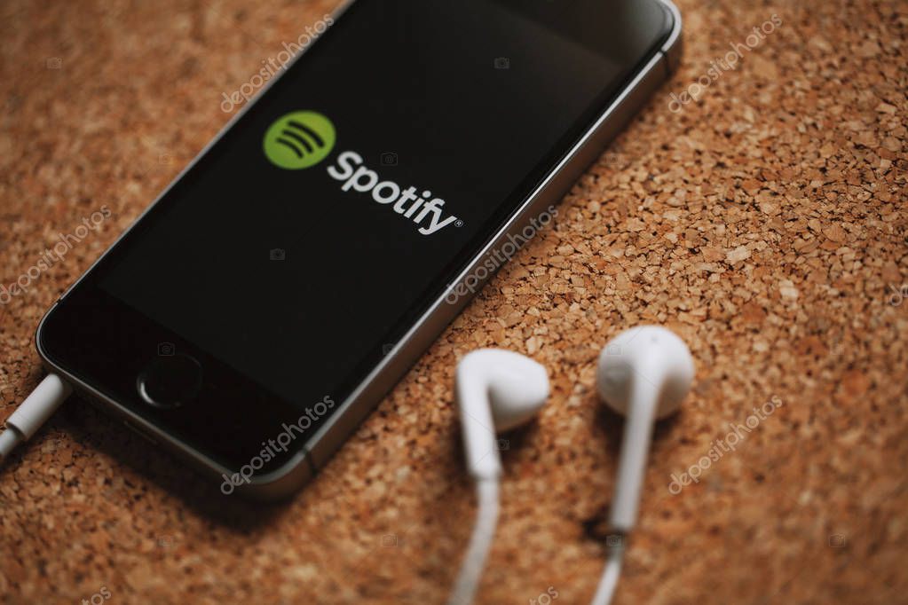 Spotify music streaming service on a smartphone screen and white earphones.