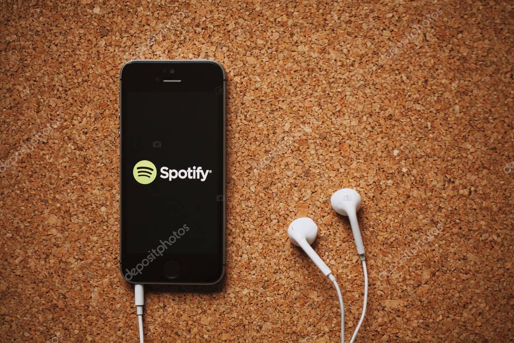 Spotify music streaming service on a smartphone screen and white earphones.