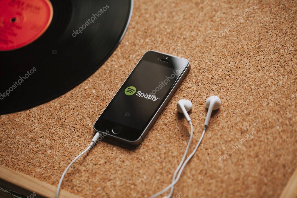 Spotify music streaming service on a smartphone screen and white earphones.