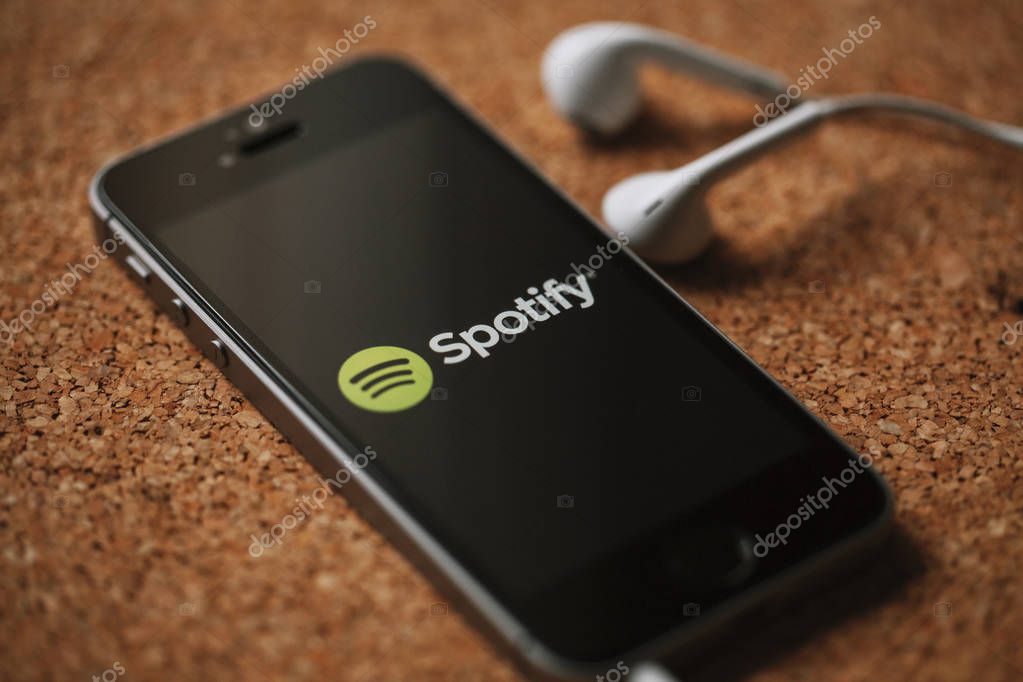 Spotify music streaming service on a smartphone screen and white earphones.