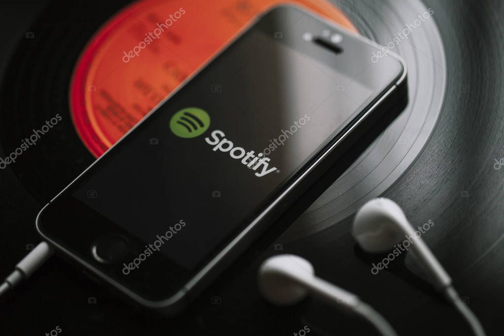 Spotify music streaming service on a smartphone screen and white earphones.