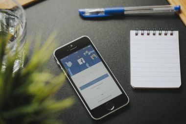 Malaga, İspanya - 6 Mart 2018: cep telefonu ile Facebook app ekranda, siyah masa başı işleri yakın üzerinde.