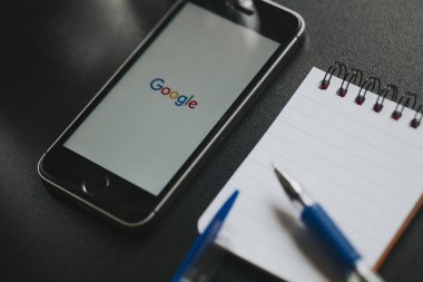 Malaga, İspanya - 6 Mart 2018: Google app bir siyah çalışma alanı diğer office malzeme ile yerleştirilen bir cep telefonu ekranında,.