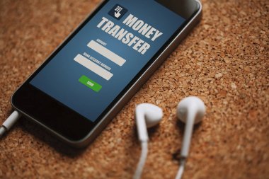 Hareket eden telefon ile para transferi uygulaması bir mantar panel ekran ve beyaz kulaklık.