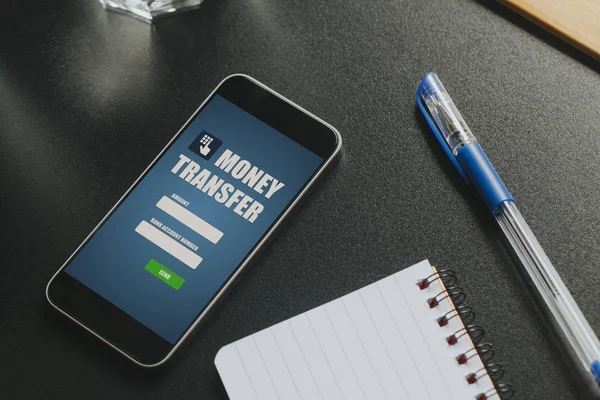 Money transfer app in a mobile phone screen over a black business table.