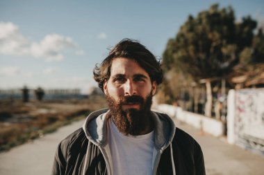Güneşin kentsel sokak stil giysileri ile bir yüz yan kameraya bakarak adam portre, genç sakallı
