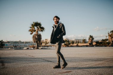 Kentsel giyim tarzı ile gün batımında açık havada yürüyen genç adam.