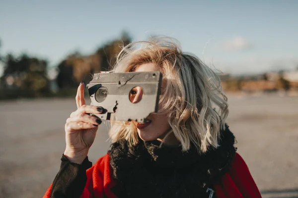 Femme alternative blonde jouant avec une bande VHS à l'extérieur au coucher du soleil. Concept de cinéaste créatif . — Photo