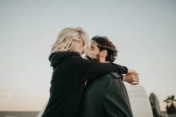 Pasangan muda yang keren mencium satu sama lain di luar ruangan sementara mereka dipeluk, selama perhentian perjalanan, dengan van mereka di latar belakang . — Stok Foto