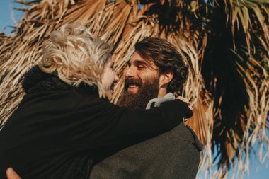 Sakallı adam gülüyor ve onun gözlerine bakmak süre gün batımında sevgilisini kucaklayan.