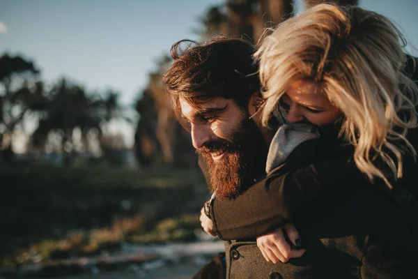 Cool indie casal se divertindo ao ar livre, enquanto ele lhe dá um piggyback . — Fotografia de Stock