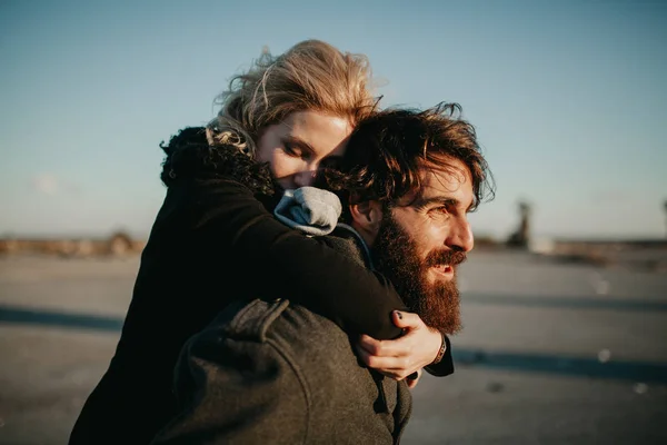 Cool indie casal se divertindo ao ar livre, enquanto ele lhe dá um piggyback . — Fotografia de Stock