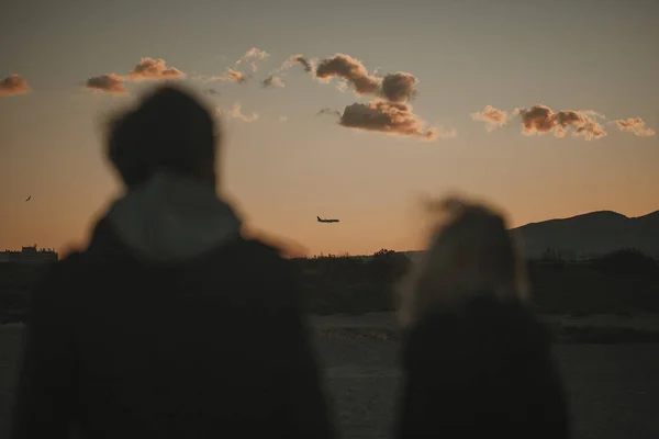 Silhouette von Mann und Frau beim Spazierengehen in der Natur, mit orangefarbenem Himmel und einem Flugzeug im Hintergrund. — Stockfoto