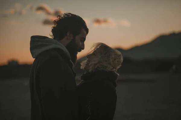 Close up retrato de casal legal olhando uns para os outros ao pôr do sol com um céu laranja no fundo . — Fotografia de Stock