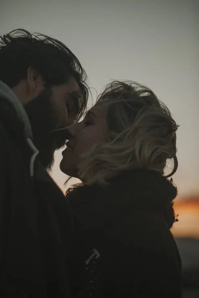 Nahaufnahme Porträt eines coolen Paares, das sich bei Sonnenuntergang küsst, mit einem orangefarbenen Himmel im Hintergrund. — Stockfoto