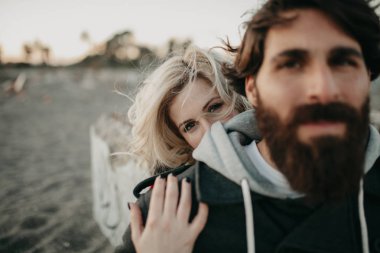 Sahilde kum oturan genç hippi çift romantik kucakladı.