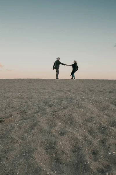 Mann und Frau gehen am Strand Sand bei Sonnenuntergang, Händchen haltend, mit dem Meer und einem blauen Himmel im Hintergrund. — Stockfoto