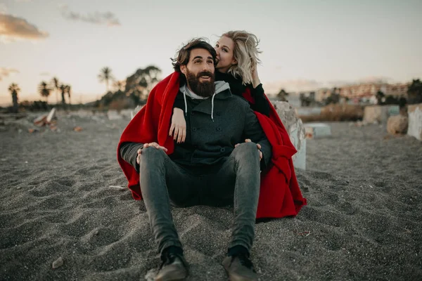 Jovem casal hipster sentado na areia da praia abraçado romanticamente . — Fotografia de Stock