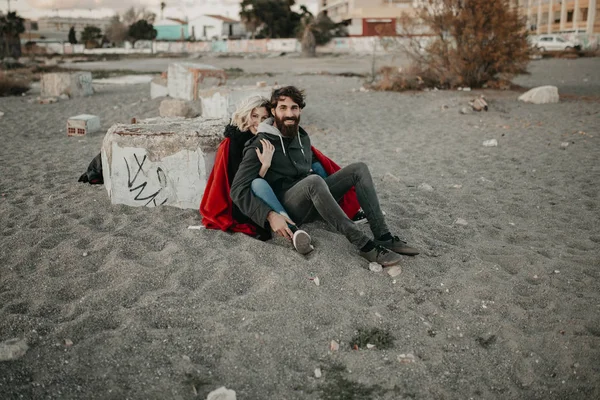 Jonge hipster paar zittend op het strand zand omarmd romantisch. — Stockfoto