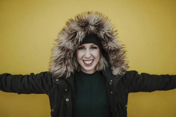 Porträt einer weißen lächelnden Frau, die eine Jacke mit Kapuze trägt, vor gelbem Hintergrund — Stockfoto