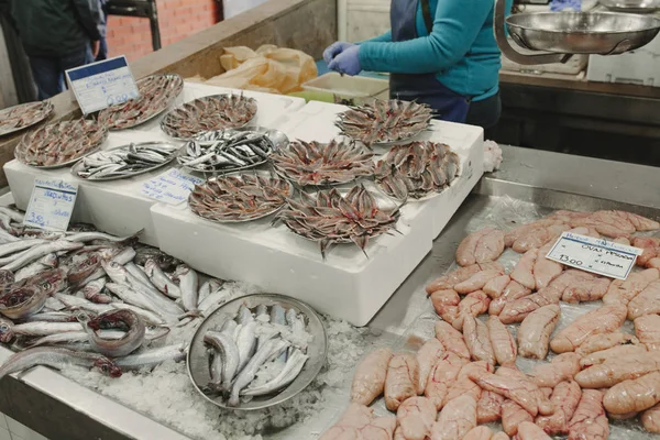 Acciughe fresche e altri pesci al mercato del pesce mentre il pescivendolo pulisce i pesci . — Foto Stock