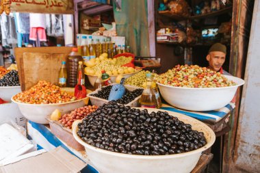 Rissani, Morocco - September 18th, 2019: Assorted olives for sell in at the foor market, and seller sitting in the background, in Rissani, Morocco