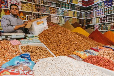 Rissani, Morocco - September 18th, 2019: Traditional stall with spices and herbs, and seller talking to the tourists, at the food market of Rissani city, Morocco.