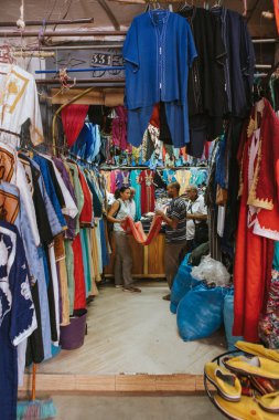 Rissani, Fas - 18 Eylül 2019: Tekstil dükkanı ve kadın ve erkek Fas 'taki Rissani pazarında kıyafet fiyatları hakkında konuşuyorlar.