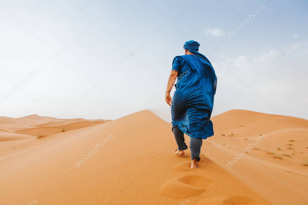 Man with classic berber clothes on walking by the desert dunes alone.