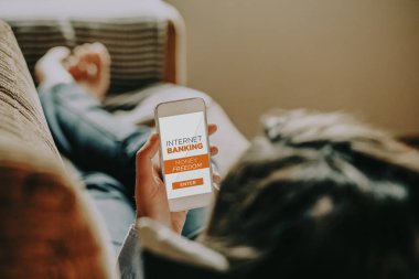 Evde dinlenirken internet bankacılığı için cep telefonu kullanan bir kadın..