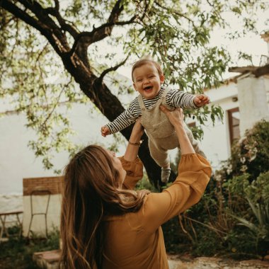 Anne oğlunu havada tutuyor ve bebek gülüyor..