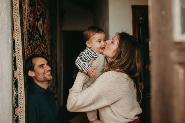 Evlerinin merdivenlerinde oturup oğullarını önemseyen sevimli bir çift. Anne bebeği öperken baba gülümsüyor..