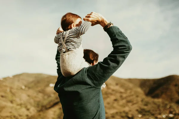 Backwards man giving a piggyback ride to his baby son outdoors.