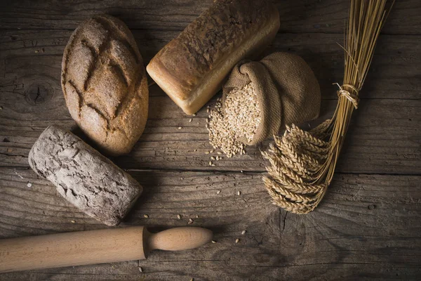 Bordo di pane su legno con sfondo spazio copia. Pani integrali marroni e bianchi natura morta composizione con spighe di grano sparse in giro. Concetto di panetteria e alimentari . — Foto Stock
